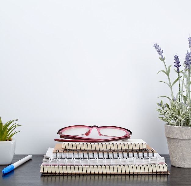 Stapel gewundene Notizbücher nahe bei einem Keramiktopf mit einer Blume auf einer schwarzen Tabelle