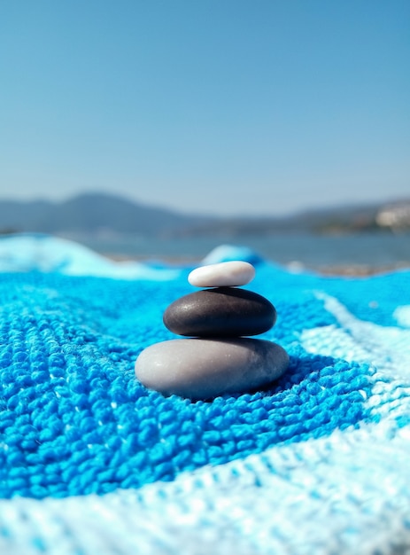 Stapel Kieselsteine auf einem blauen Strandtuch an einem sonnigen Tag Viel Spaß und Entspannung am Strand Reisen Sommerferienkonzept Graue schwarze weiße glatte Kieselsteine im Stapel