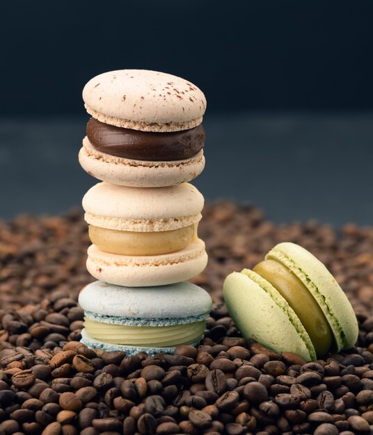 Stapel mehrfarbiger Macarons liegt auf gerösteten Kaffeebohnen, schwarzer Oberfläche, köstlichem und exquisitem Dessert