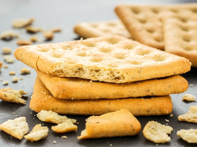 Stapel quadratischer Cracker mit Stücken und Krümeln auf Schiefergrau