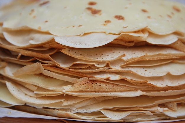 Stapel russischer Pfannkuchen auf einem runden weißen Teller auf schwarzem Hintergrund. Pfannkuchentag in Russland. Appetitanregende russische Pfannkuchen für Maslenitsa Karneval Fasching. Nahaufnahme