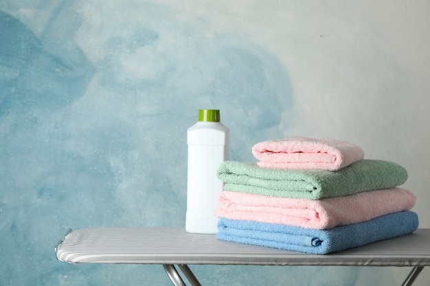 Stapel sauberer Handtücher und Waschmittel auf Bügelbrett,