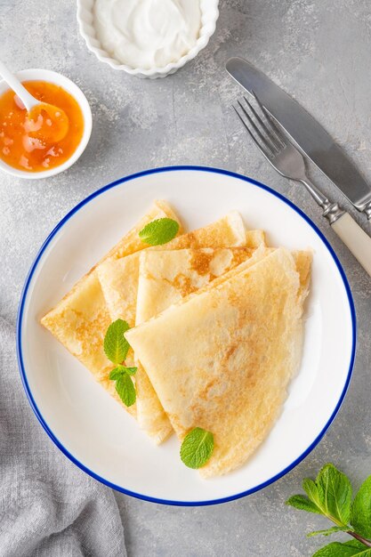 Stapel traditioneller dünner Pfannkuchen oder Crêpes auf einem Teller mit Honig und Sauerrahm. Kopierraum