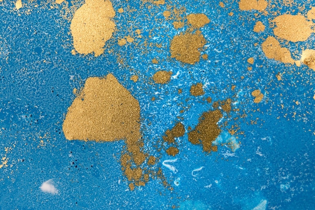 Stapel von goldenen Pailletten auf blauem flüssigem Tintenhintergrund. Abstrakte gießende Farbe