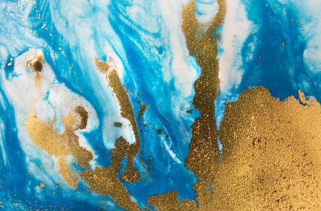 Stapel von goldenen Pailletten auf blauen Farbflecken. Abstrakte gießende Farbe