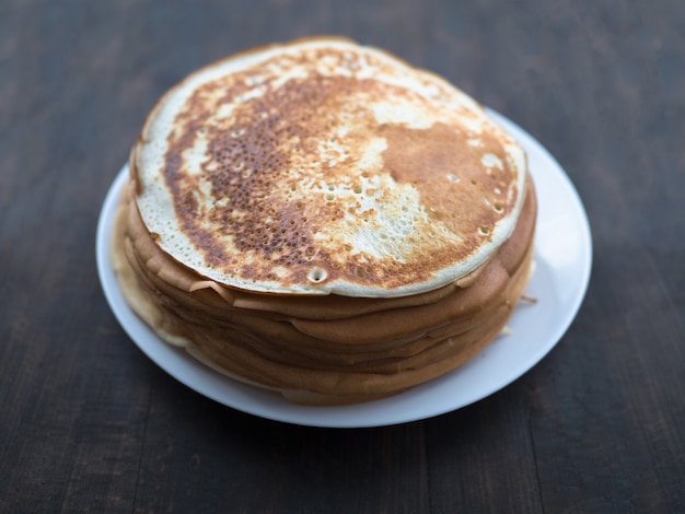 Foto stapel von hausgemachten pfannkuchen auf einem weißen teller auf einer schwarzen oberfläche