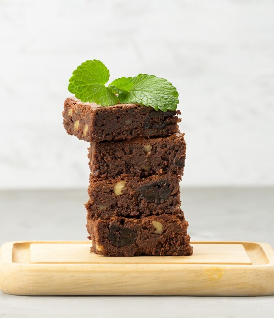 Stapel von quadratisch gebackenen Brownie-Schokoladenkuchenstücken auf Holzbrett, köstliches Dessert