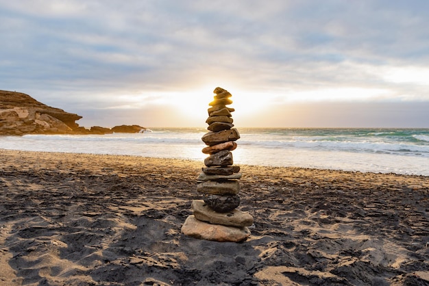 Stapel von Steinen balancieren an einem Strand vor einem bewölkten Himmel bei Sonnenuntergang TimeZen ConceptCopy Space