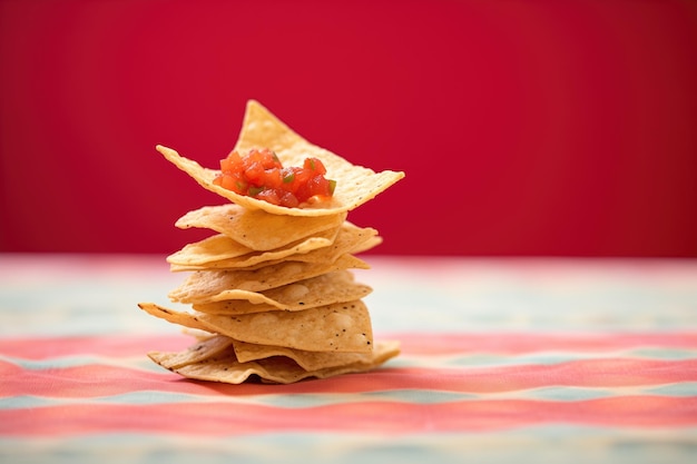 Stapel von Tortilla-Chips mit einem einzigen Chip, der in roten Salsa-neutralen Tischtuch getaucht ist