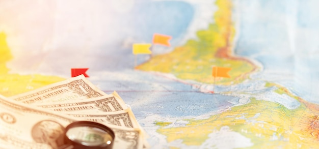 Stapel von US-Dollar-Bargeldlupe und Stecknadel-Reisekonzept Ziel, das mit einer Stecknadel auf der Karte markiert ist
