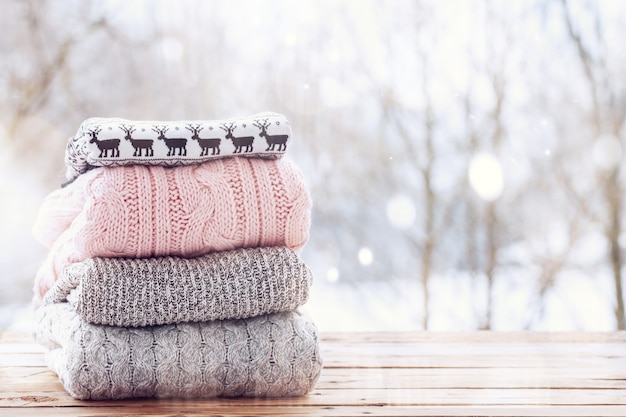 Stapel von Wollstrickkleidung auf hölzernem Tisch auf Winterhintergrund