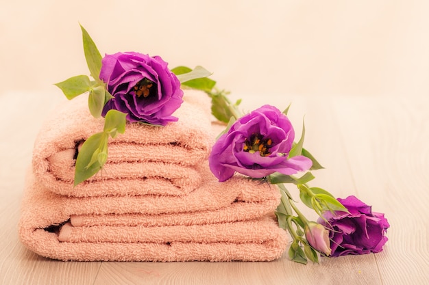 Stapel weiche Frotteehandtücher mit violetten Blüten auf rosafarbenem Hintergrund.