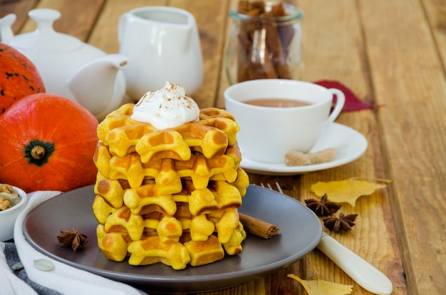 Stapel würziger Kürbiswaffeln auf einem dunklen Teller mit Karamellsauce und Schlagsahne