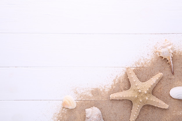 Starfish und Muscheln mit Sand auf weißem hölzernem mit Kopienraum. Sommer-Konzept