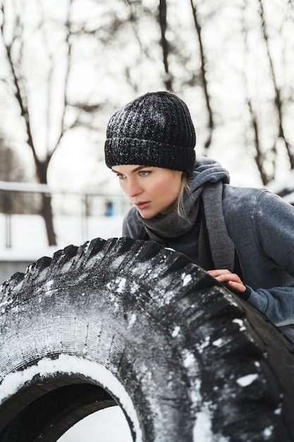 Starke athletische Frau, die während ihres Trainings an verschneiten und kalten Wintertagen mit einem Reifen trainiert