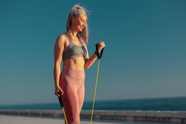 Starke Frau in Sportbekleidung, die auf Sportgelände mit Fitness-Widerstandsbändern trainiert