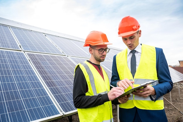 Starke männliche Arbeiter kommen gut mit der Aufgabe über den Plan der Installation von Sonnenkollektoren zurecht. Das Konzept des grünen Stroms und seine Arbeit