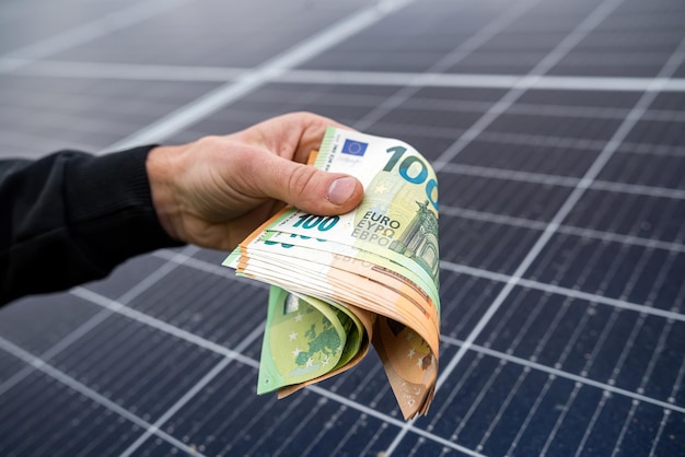 Starke männliche Hände in einer blauen Jacke halten Euro-Banknoten vor Sonnenkollektoren Konzept des sparsamen grünen Stroms