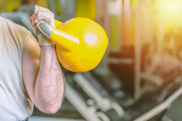 Starke männliche Hand mit gelbem kettlebell im Turnhalleneignungssportzentrum.