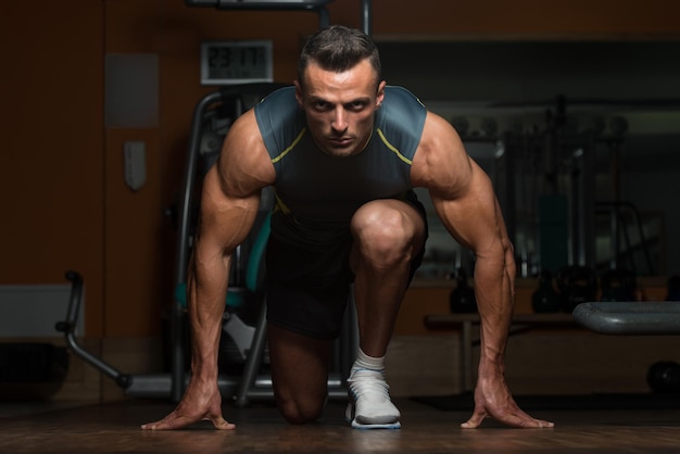 Starke muskulöse Männer, die auf dem Boden knien, fast wie Sprinter-Ausgangsposition