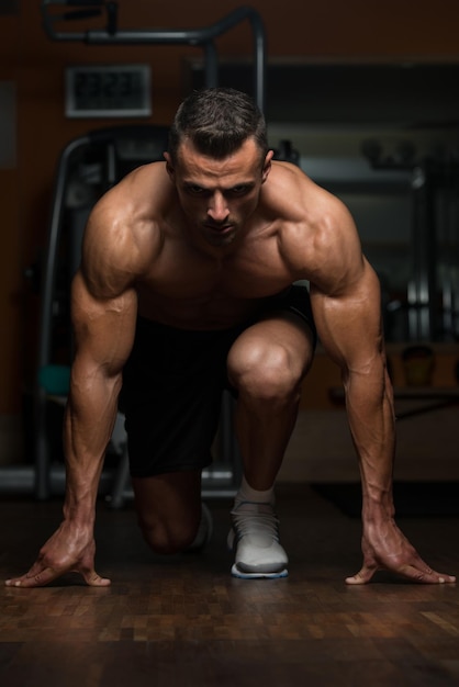 Starke muskulöse Männer, die auf dem Boden knien, fast wie Sprinter-Ausgangsposition
