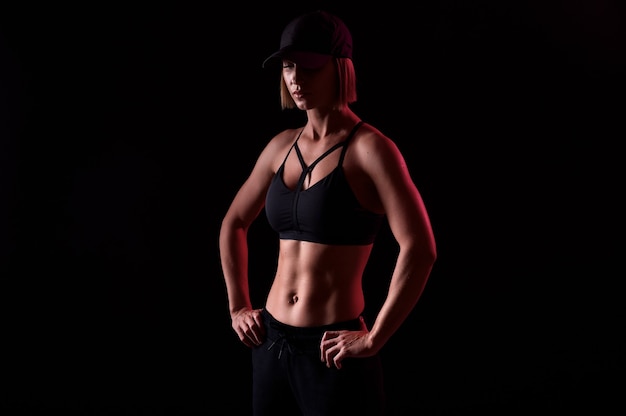 Starke Sportlerin, die Sport-BH mit muskulösem Bauch trägt, hört Musik in Kopfhörern auf schwarzem Hintergrund. Perfekte Körperform