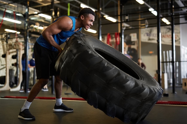 Starker afrikanischer Mann, der Reifen im Fitnessstudio umdreht