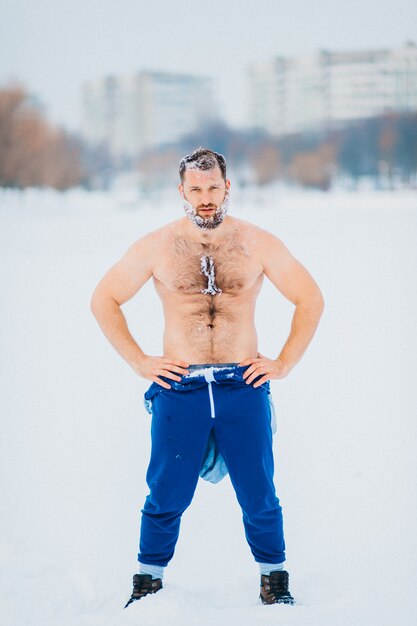 Starker Bodybuilder bedeckt mit der Schneeaufstellung im Freien am schneebedeckten Tag des Winters