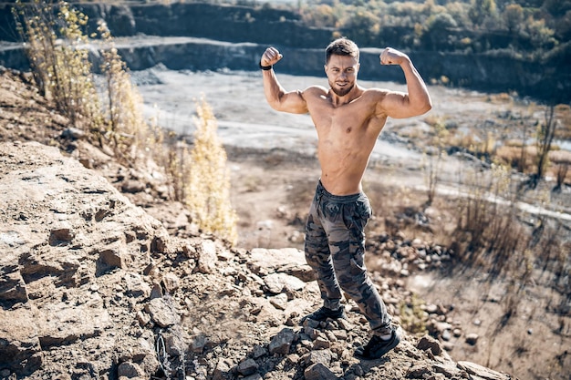 Starker Bodybuilder, der auf Felshintergrund steht und mit nacktem Oberkörper posiert Steinhintergrund über dem Mann Beschnittene Ansicht