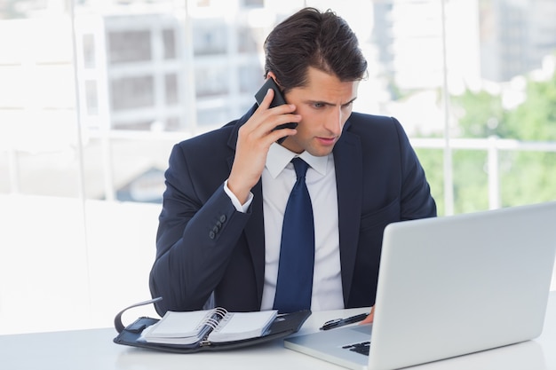 Starker Geschäftsmann, der einen Telefonanruf hat und an seinem Laptop arbeitet