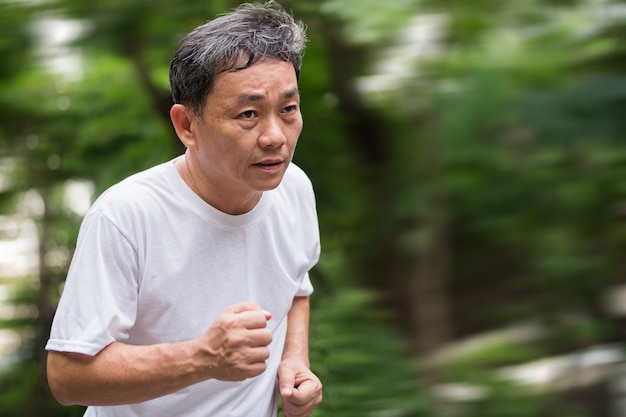 Starker gesunder Mann des älteren oder mittleren Alters, der Joggingsprinten im gesunden Lebensstilkonzept des Parks läuft