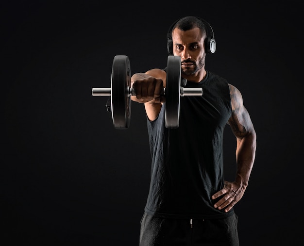 Starker hübscher Sportmann, der Gewichtheben, hörende Musik macht und die Schultern trainiert