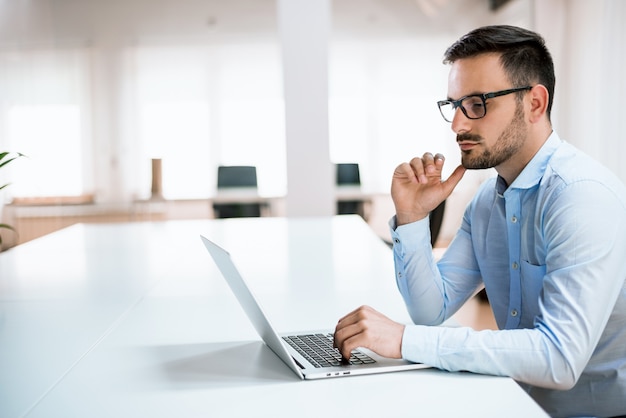 Starker junger Geschäftsmann schreibt Informationen über seinen Laptop im Büro.