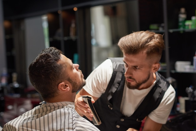 Starker männlicher Friseur, der Trimmer in den Händen hält.