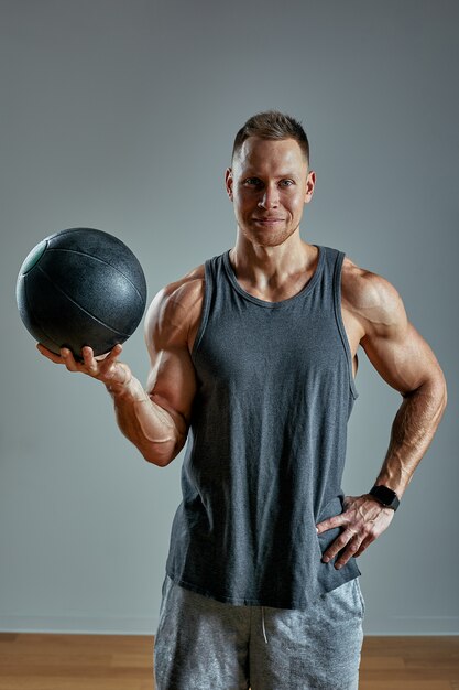 Starker Mann, der Übung mit MED-Ball tut. Foto der perfekten Konstitution des Mannes auf grauem Hintergrund. Kraft und Motivation.