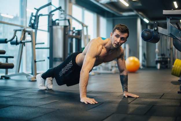 Starker Mann mit nacktem Oberkörper, der Liegestütze im Fitnessstudio macht