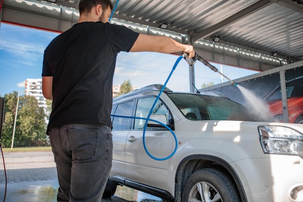 Starker Mann wäscht Auto bei Selbstwaschanlage im Sommer im Freien