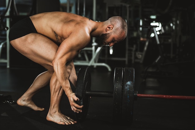 Starker muskulöser Mann, der Langhantel vorbereitet und sich auf das Gewichtheben im Fitnessstudio vorbereitet.