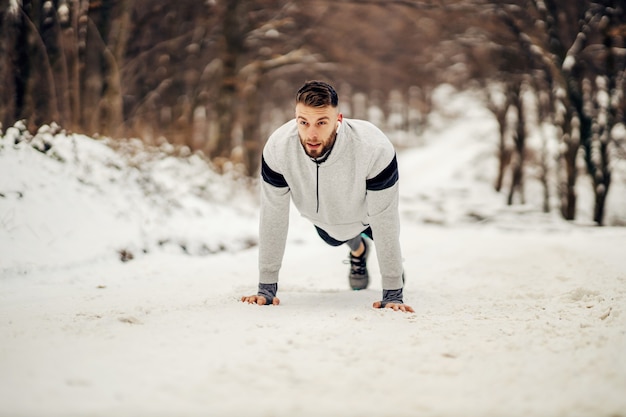 Starker Sportler, der im Winter Liegestütze in der Natur auf verschneitem Weg macht. Gesunder Lebensstil, Winterfitness, Kraftübungen