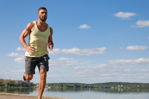 Foto starker sportmann, der beim training in der nähe der stadt am fluss joggt.