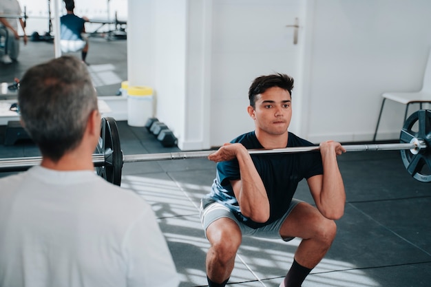 Foto starker und muskulöser junger mann in seinen 20ern, der mit der motivation eines personal trainers krafttraining für das gewichtheben macht