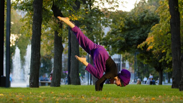 Starkes, aktives muslimisches Mädchen im Hijab, Yogi-Sportlerin beim Yoga-Training im Park auf grünem Rasen