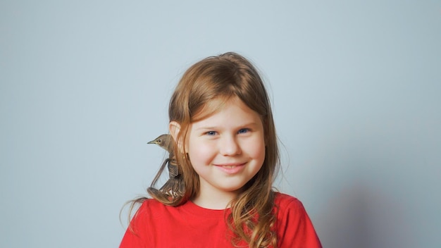 Starling adulto enclavado sentado en el hombro de una niña sonriente Retrato de un niño feliz en un pájaro cantor de primavera gris