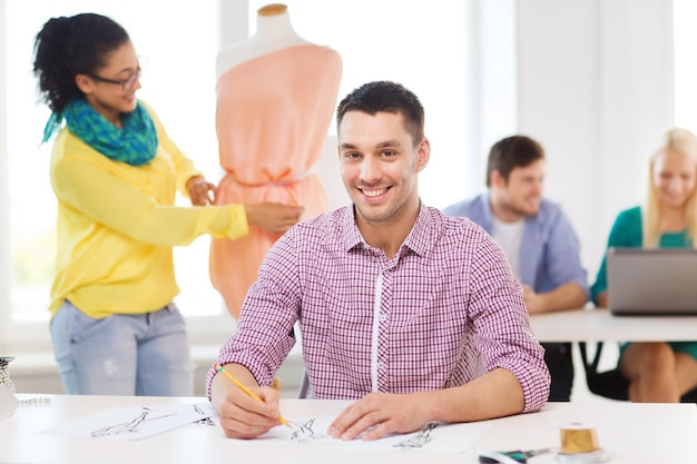 Start-, Bildungs-, Mode- und Bürokonzept - lächelnde männliche Zeichnungsskizzen und weibliche Anpassungskleider auf Mannequins im Büro