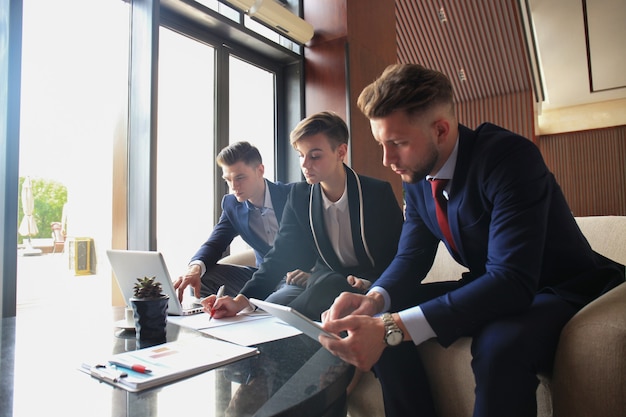 Startup-Business-Team bei Treffen in modernen, hellen Büroräumen, Brainstorming, Arbeiten an Laptop und Tablet-Computer