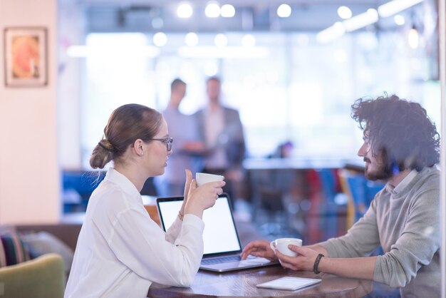 Startup-Geschäftsleute, die sich mit einem Laptop auf das nächste Meeting vorbereiten, während sie Kaffee trinken und Ideen im Kreativbüro diskutieren