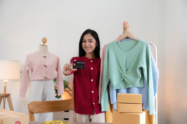 Startup pequeña empresaria empresaria PYME mujer asiática embalaje tela en caja Mano sujetando tarjeta de crédito