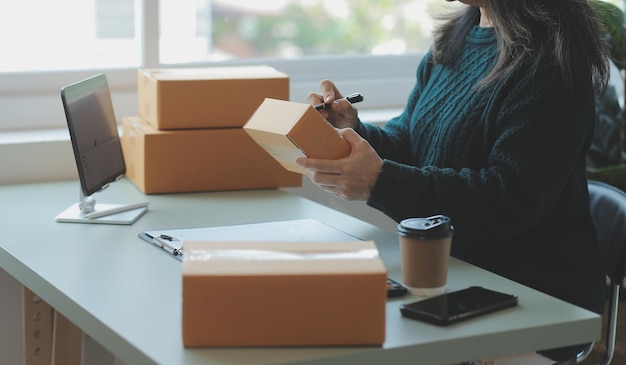 Startup PME empreendedor de pequenas empresas de mulher asiática freelance usando um laptop com caixa Mulher asiática de sucesso alegre, sua mão levanta caixa de embalagem de marketing on-line e entrega o conceito de ideia de PME