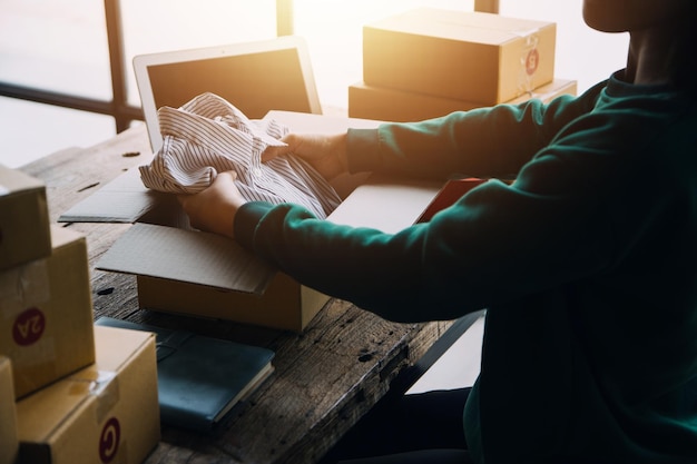 Startup PYME pequeña empresa emprendedora de freelance mujer asiática con delantal usando portátil y caja para recibir y revisar pedidos en línea para prepararse para empaquetar vender a los clientes en línea ideas de negocios sme