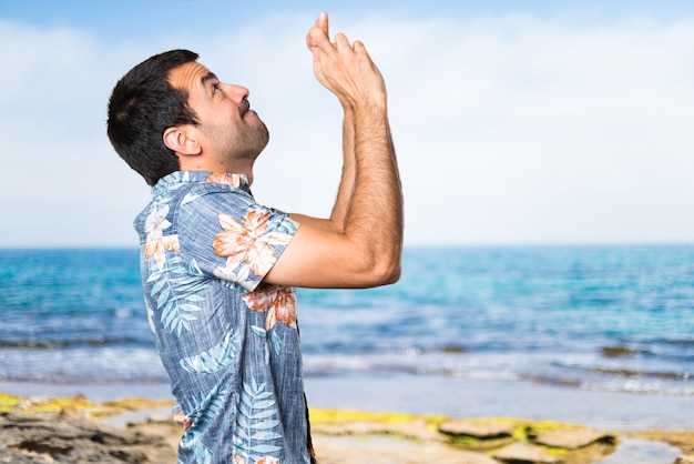 Stattlicher Mann mit Blumentopf mit den Fingern am Strand